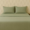 Full view of a bed made with sage green sheets and pillows, styled in a cozy spring bedroom.